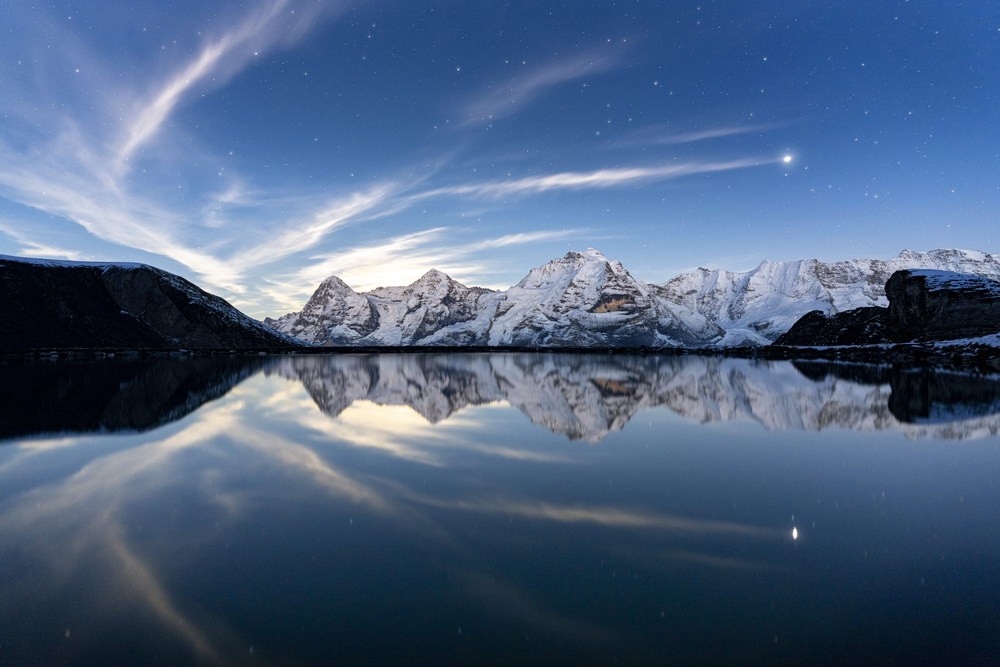 Abendhimmel mit Sternen und Wolken über den schneebedeckten Gipfeln am Bernsee