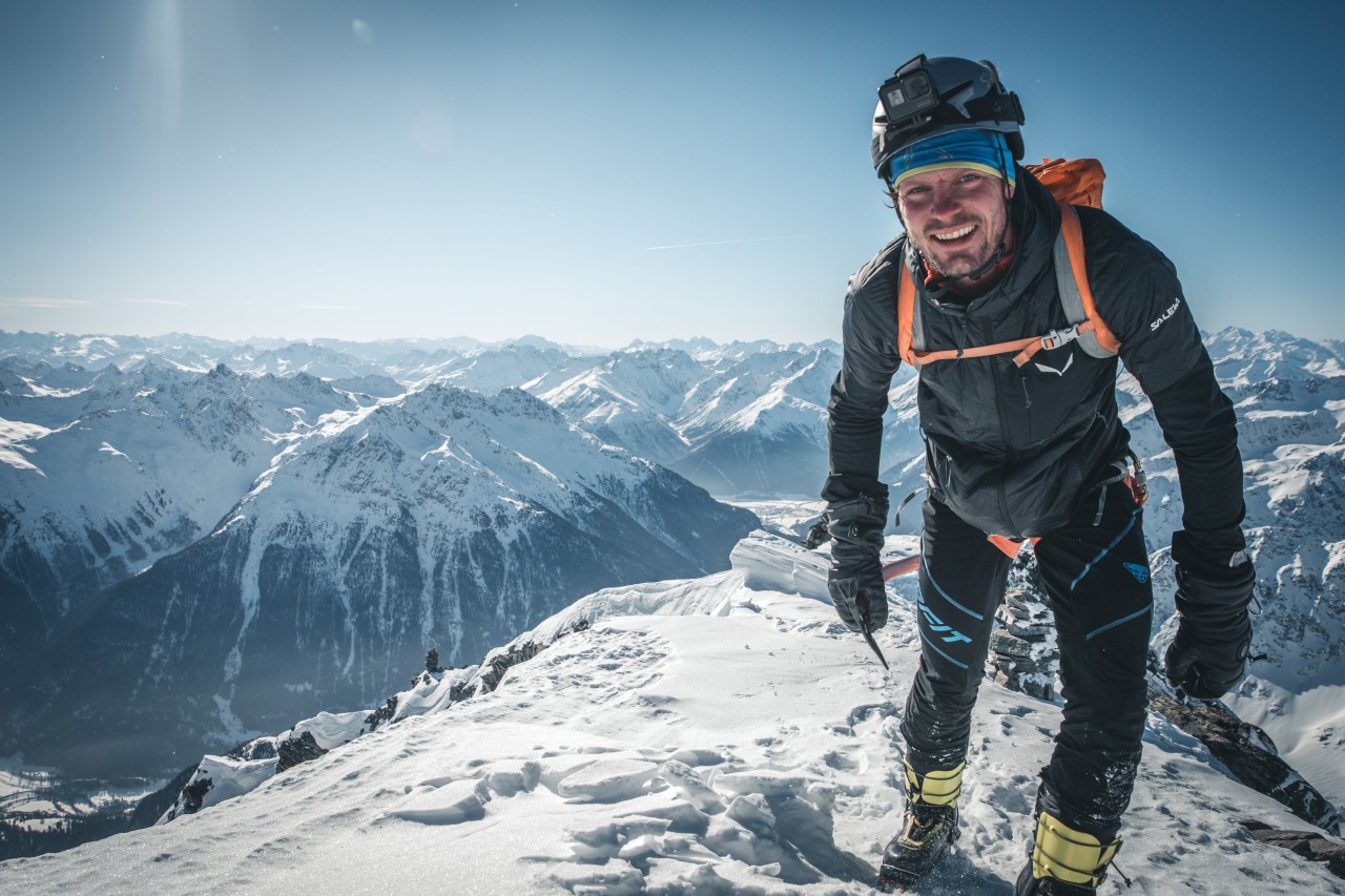 Mann in den Bergen trägt Winterliche Ausrüstung und lächelt in die Kamera