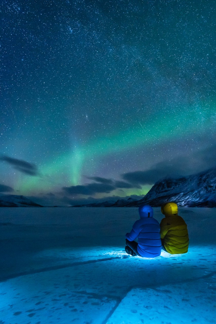 2 personas con ropa de invierno observando la aurora boreal