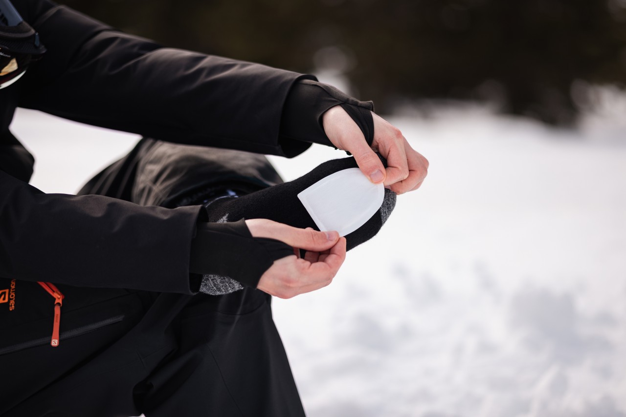 Sitzende Person im Winter klebt sich einen Fußwärmer auf den Socken