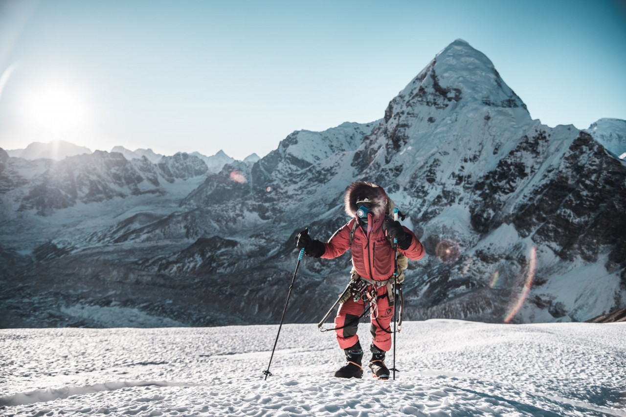 Hombre con ropa de expedición camina con bastones en la alta montaña