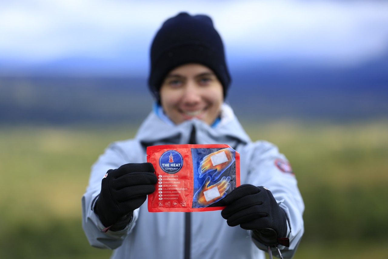 Woman with winter clothes shows a hand warmer to the camera