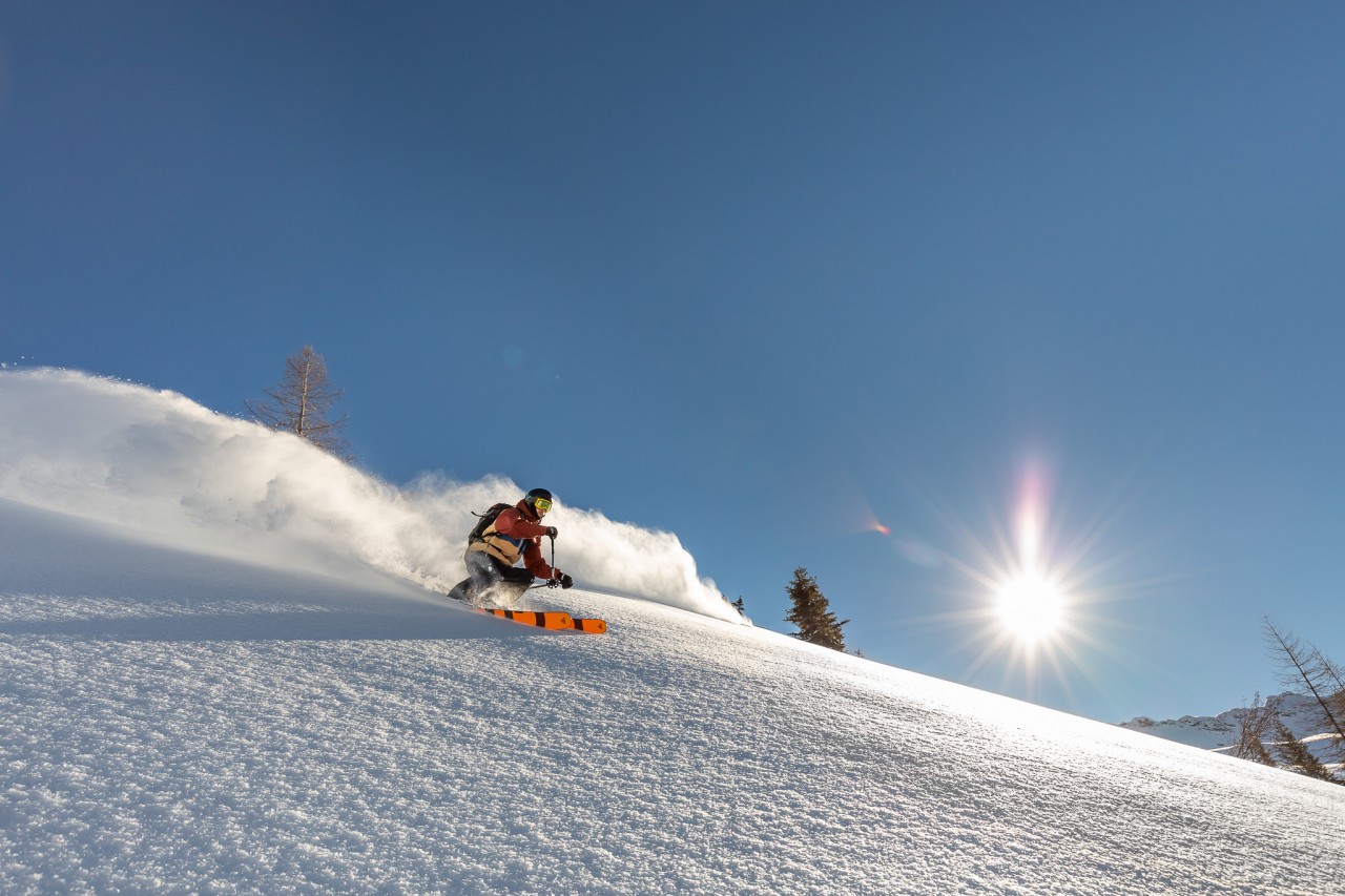Skifahrer fährt bei Sonnenschein die Piste hinunter