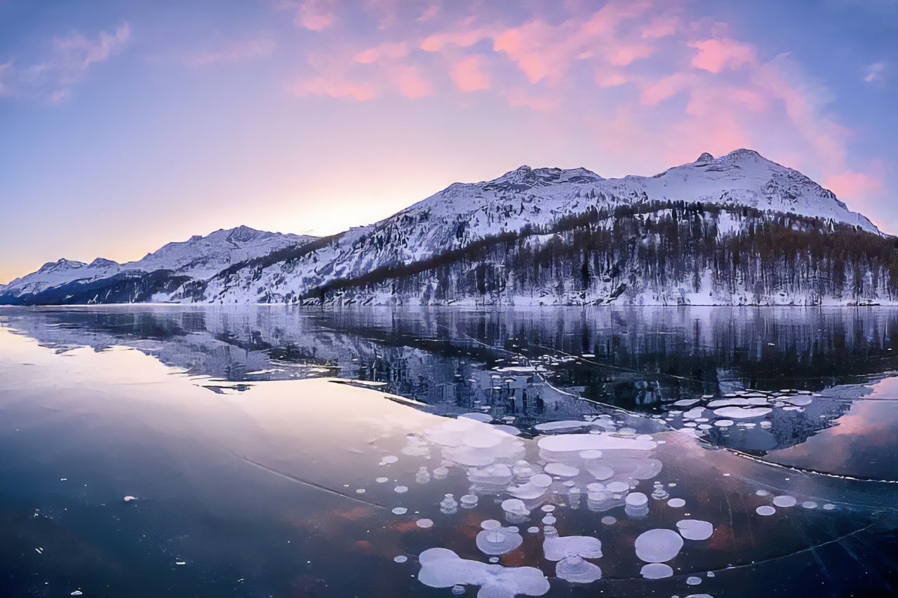 Eisblasen am zugefrorenen Silsersee mit rosa Sonnenuntergang auf den Bergen