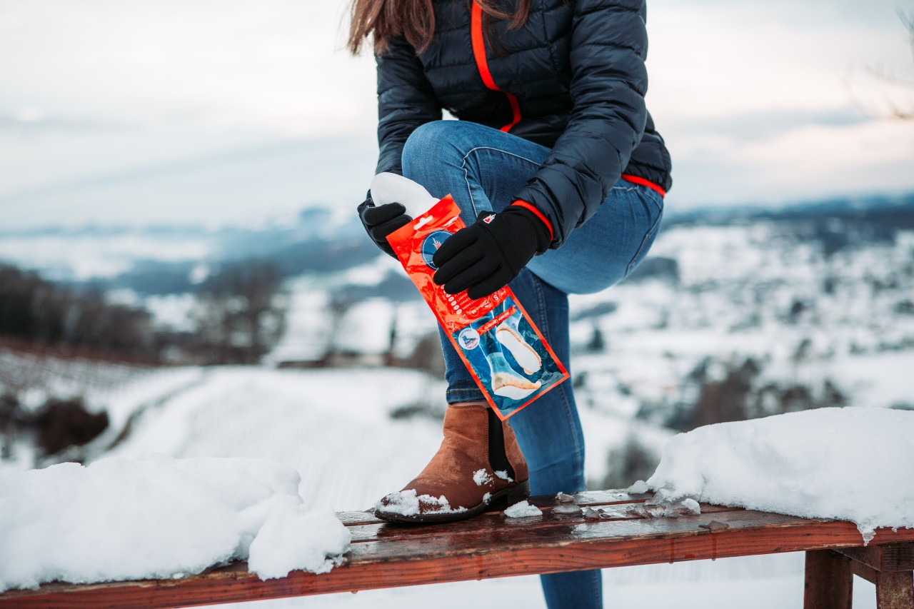 Mujer en paisaje invernal lleva guantes y saca las plantillas calentadoras del paquete