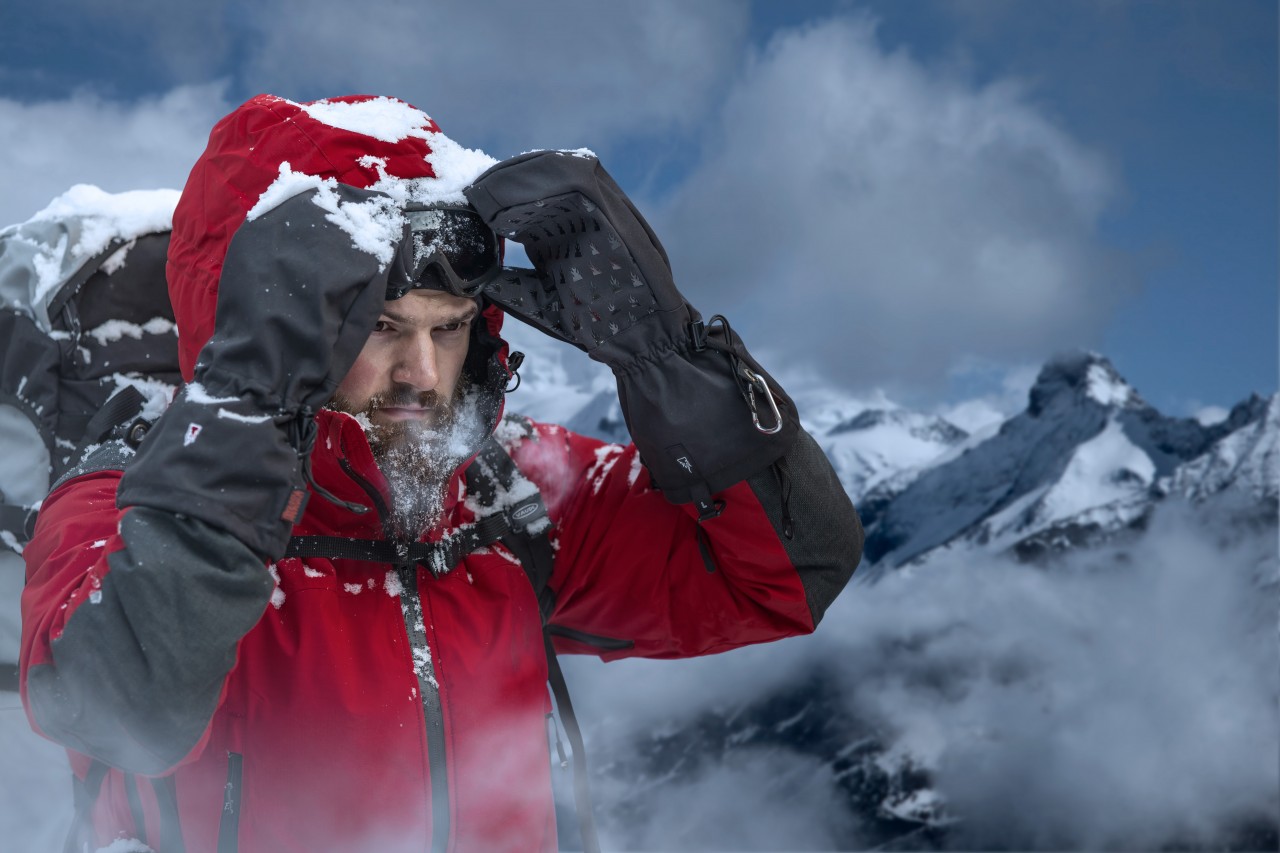 man in the mountains in extreme cold wearing over mittens