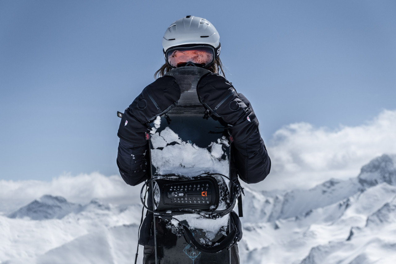 Frau in den verschneiten Bergen hält ihr Snowboard vor sich
