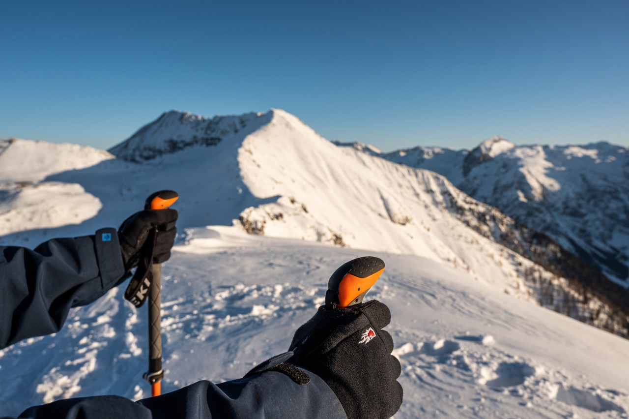 Person hält mit Fingerhandschuhen Skistöcke am Berg