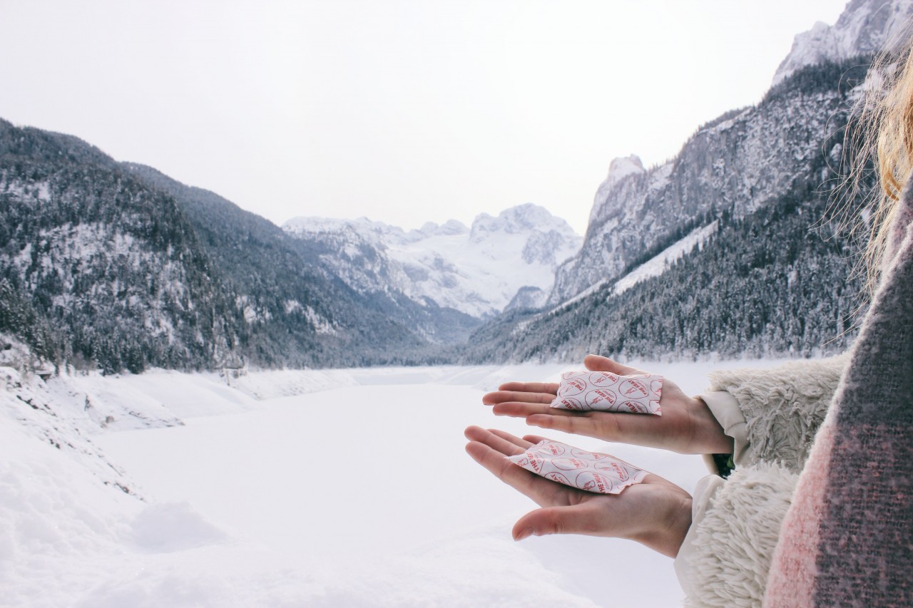 Woman holding hand warmer with snow covered mountains in background