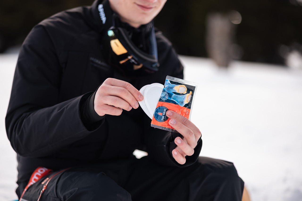 Man with goggles around the neck takes toe warmers out from the package