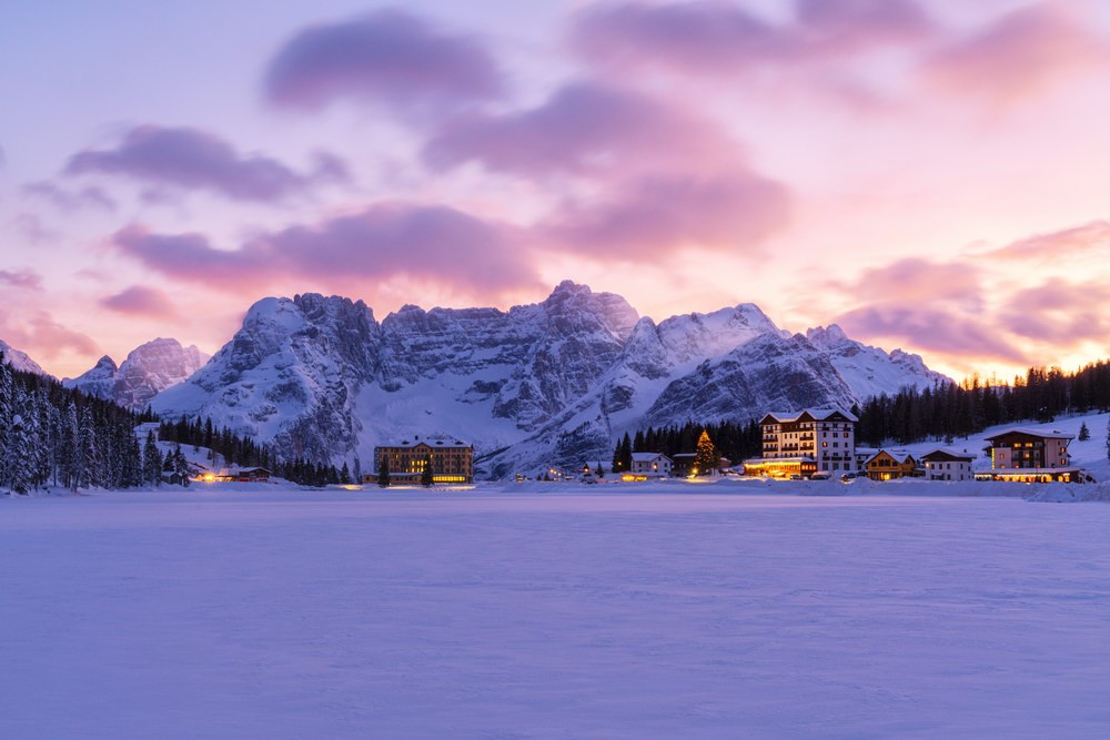 Coucher de soleil rose avec des hôtels illuminés sur le lac enneigé de Misurina