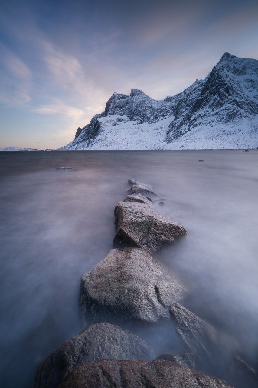 Long time exposure in Norway with rocks in the foreground and mountains in the background.