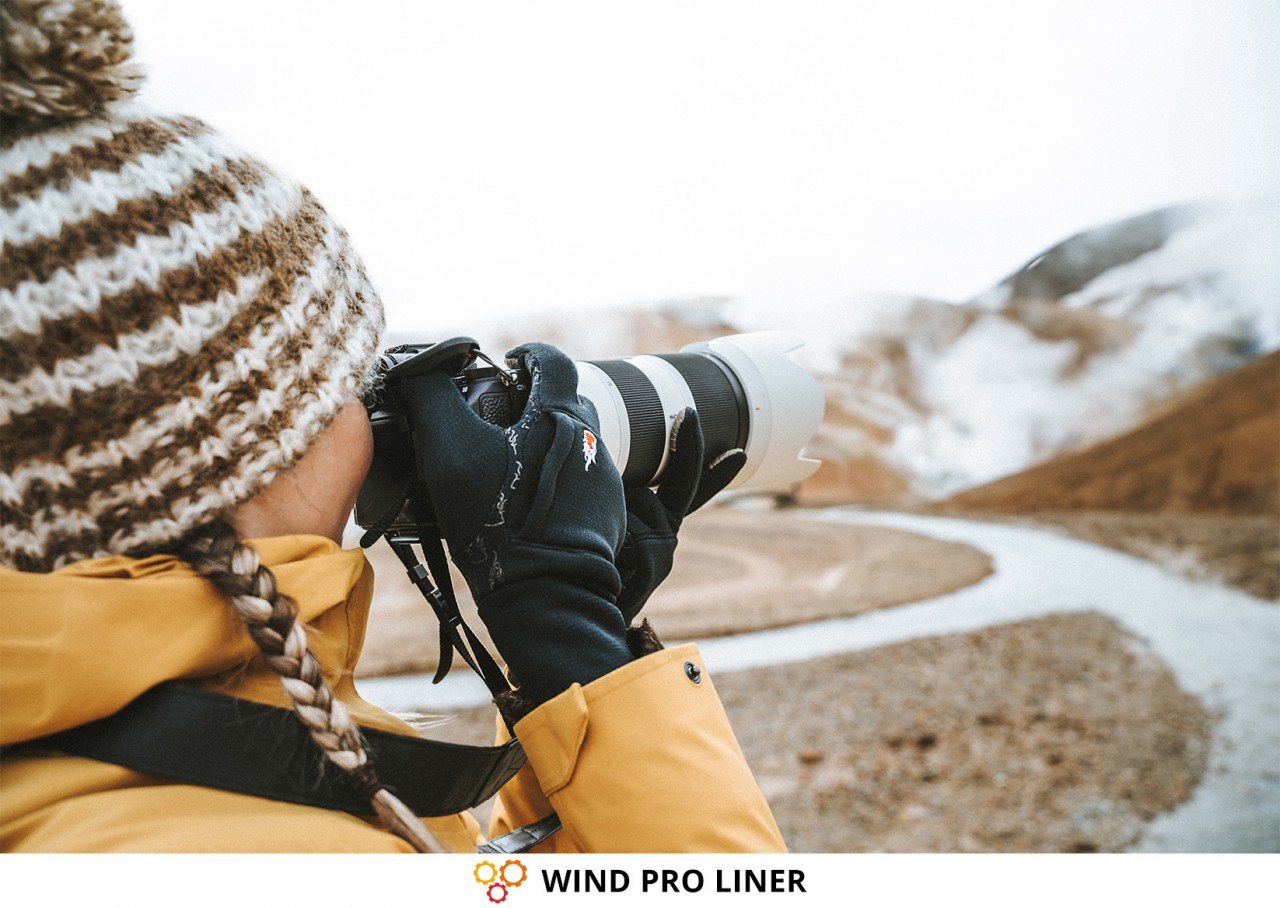 Fotografin mit süßer Mütze und gelber Jacke, die in der Kälte mit Fotohandschuhen fotografiert