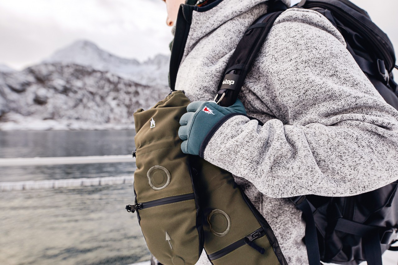 Primer plano de una fotógrafa con guantes liner, manoplas verdes y mochila fotográfica