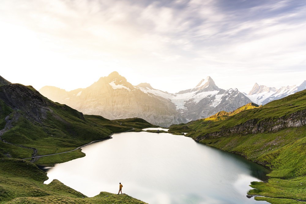 Man on the edge of a mountain lake surrounded by green mountain peaks. 