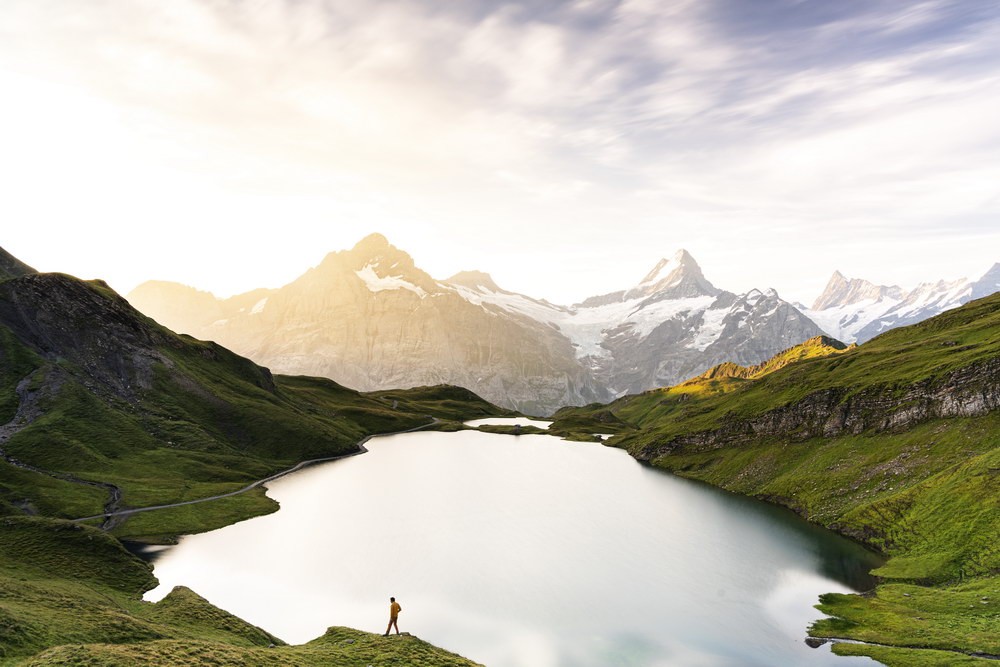 Homme au bord d'un lac de montagne entouré de sommets verdoyants