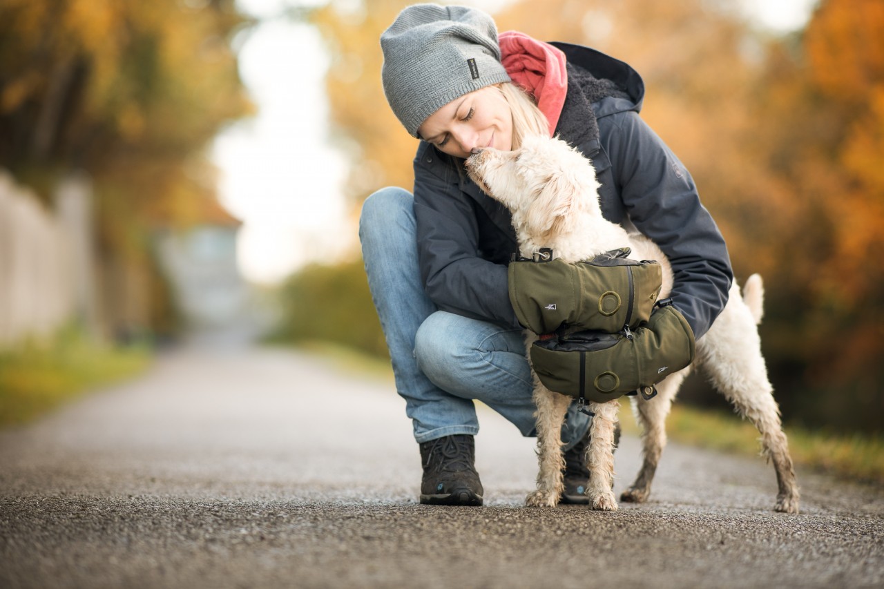 Woman kneels next to her dog, hugging him while wearing mittens