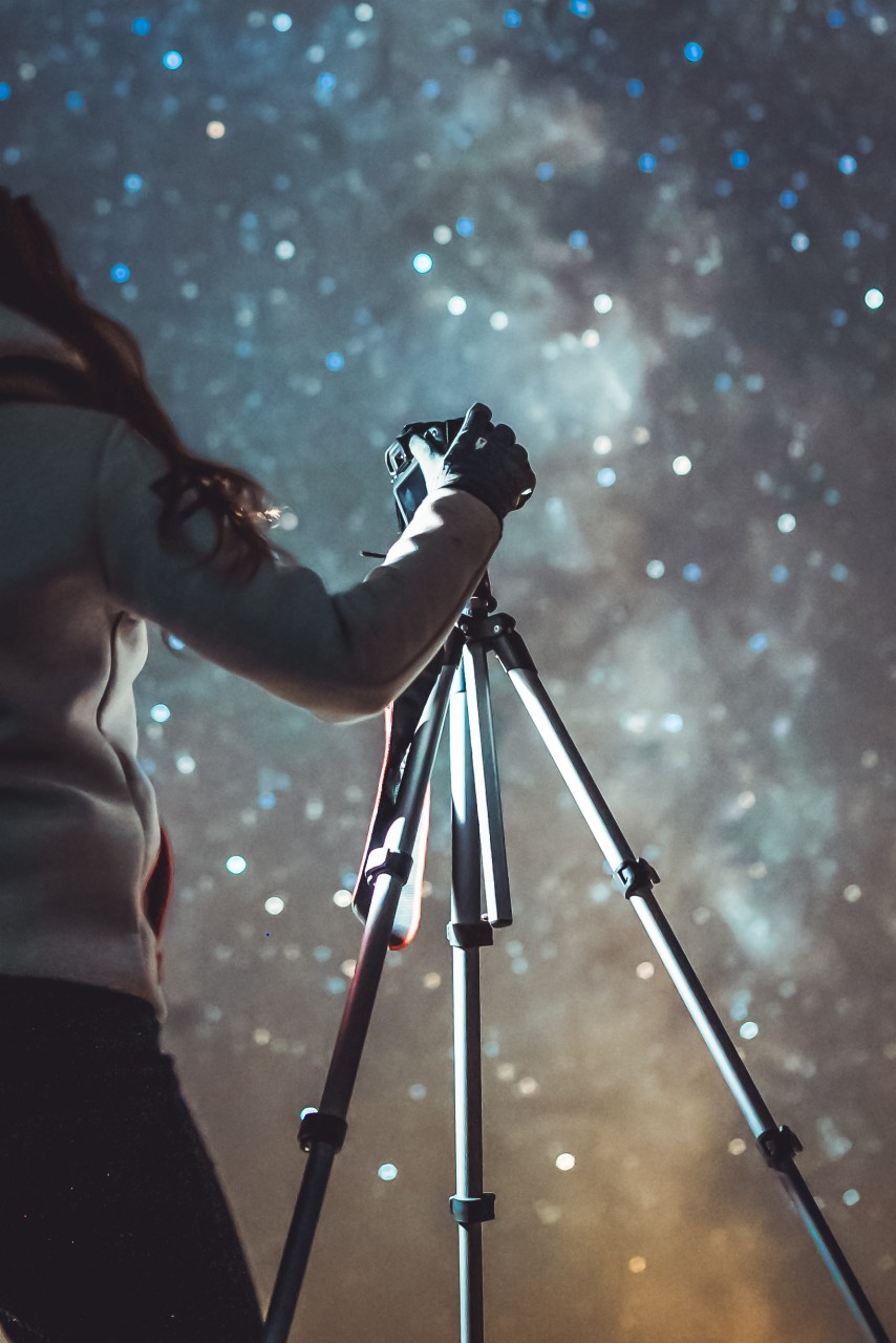 Fotógrafo con guantes sosteniendo una cámara sobre un trípode bajo un cielo nocturno gris