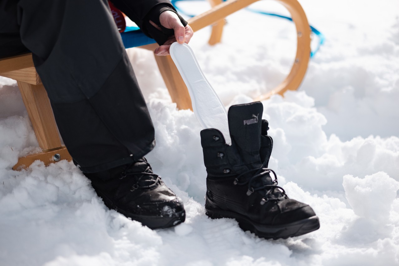 Person sitzt auf einem Schlitten und legt einen Sohlenwärmer in den Schuh