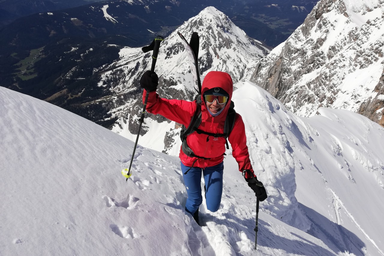 Femme en montagne faisant de l'escalade avec des skis sur le dos