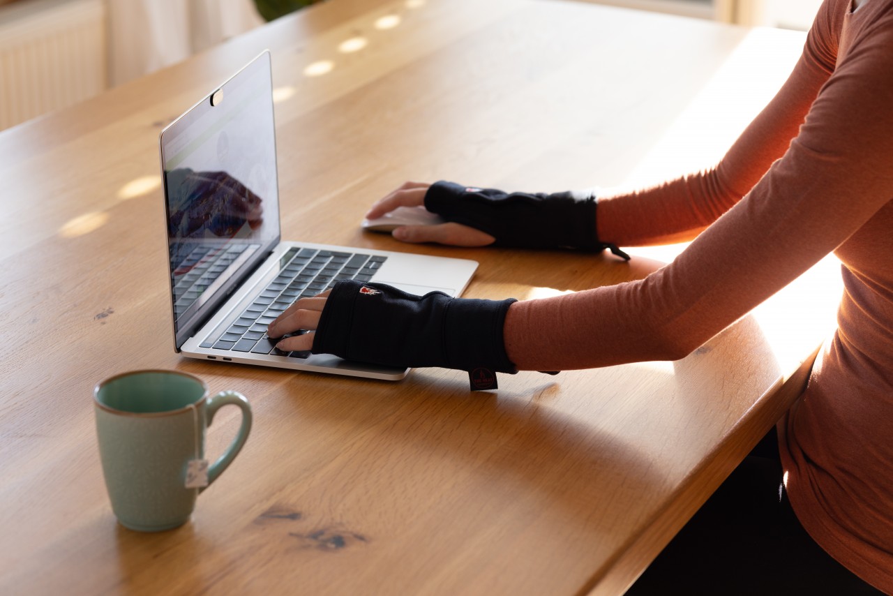 Persoon die achter de laptop zit en vingerloze handschoenen draagt