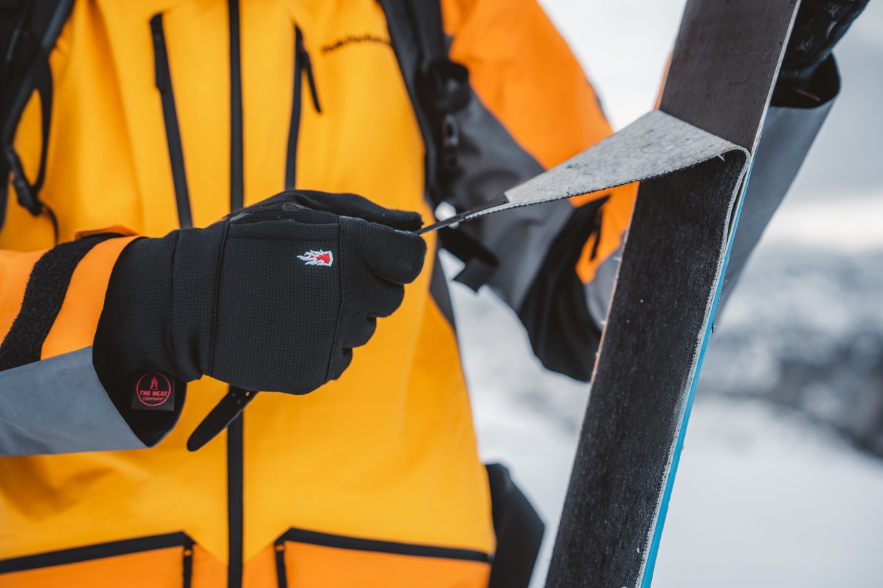 Persoon met ski-jas trekt een folie van zijn toerski's